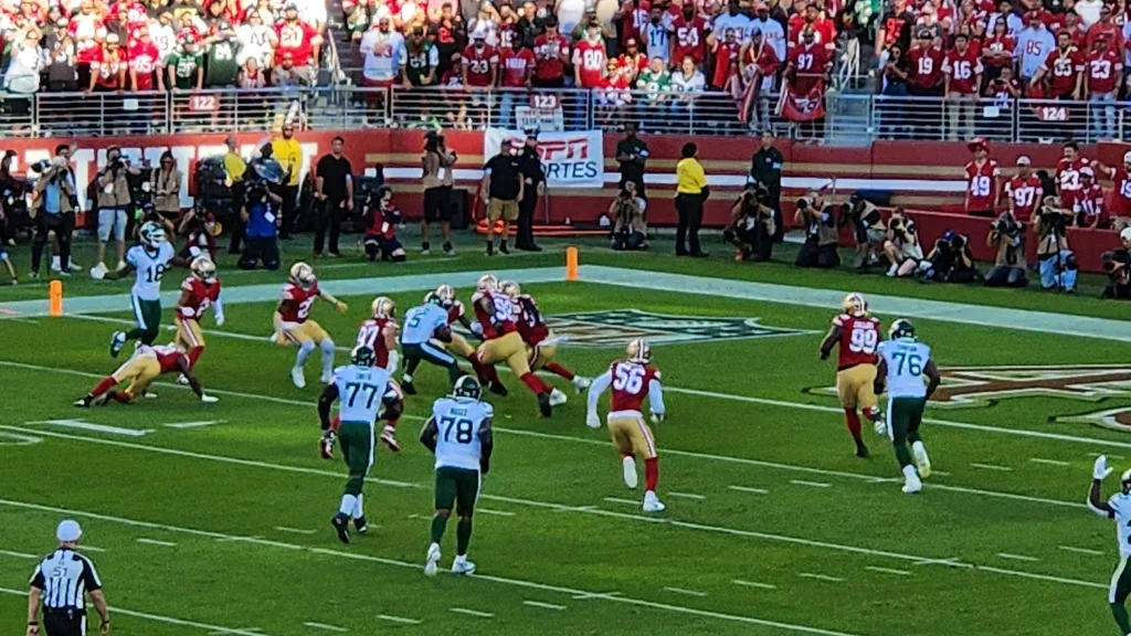 American football game in progress with players converging near midfield in a packed stadium.