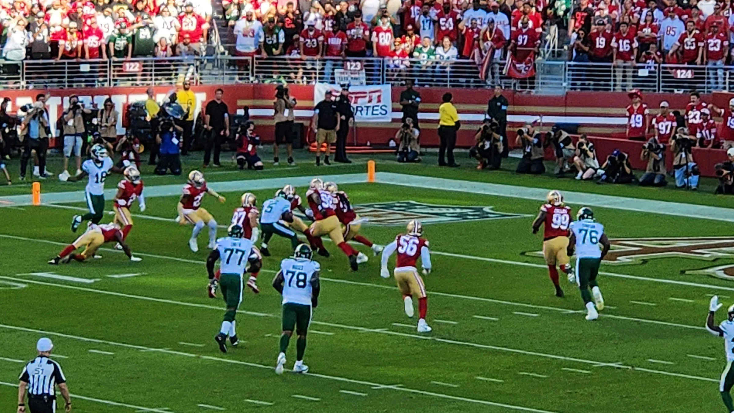 American football game in progress with players converging near midfield in a packed stadium.