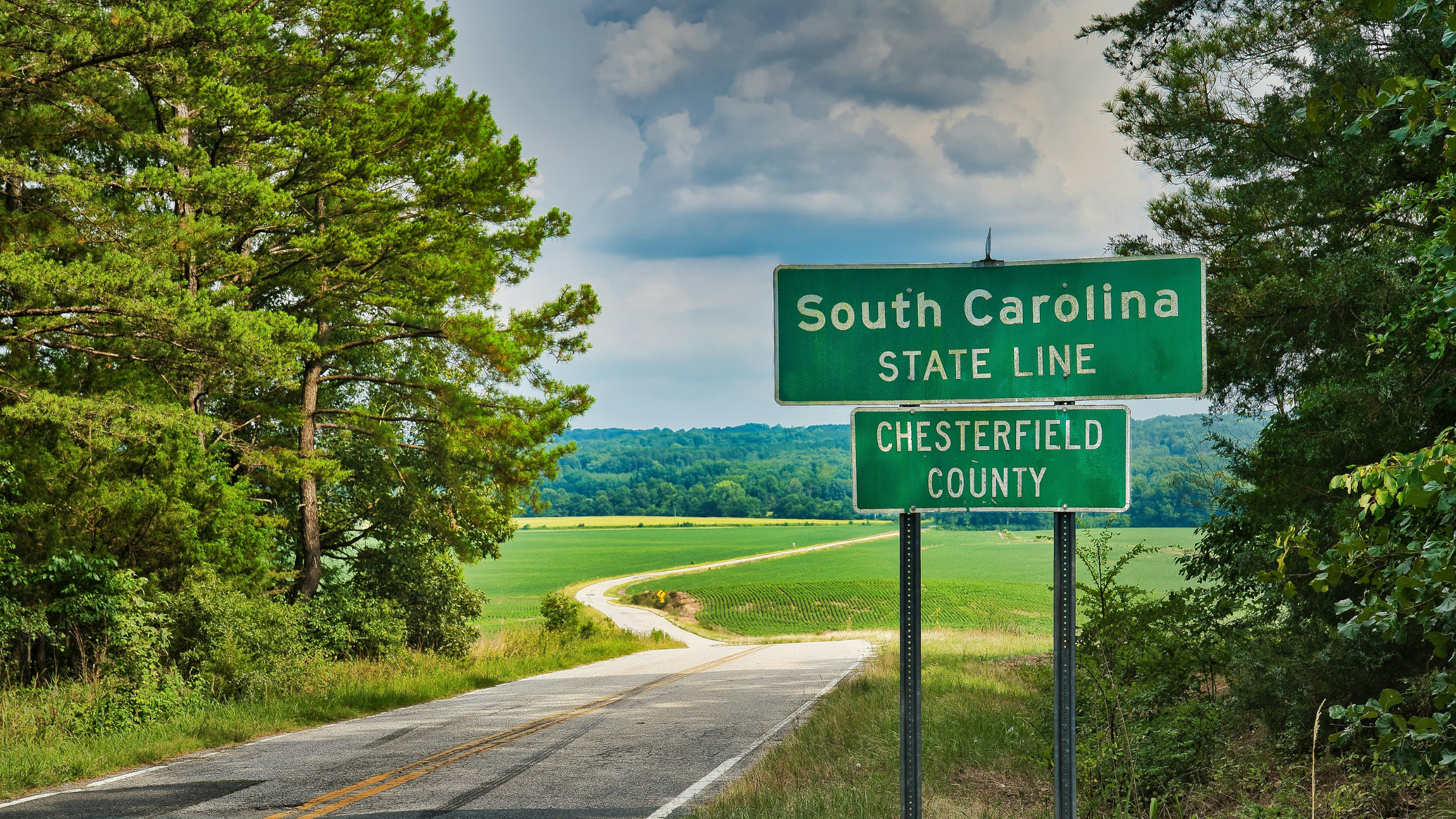 South Carolina state line road sign beside a rural road and open countryside.