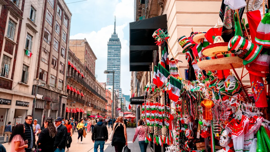 Busy Mexico City street lined with shops, pedestrians, and Mexican-themed souvenirs beneath the Torre Latinoamericana.