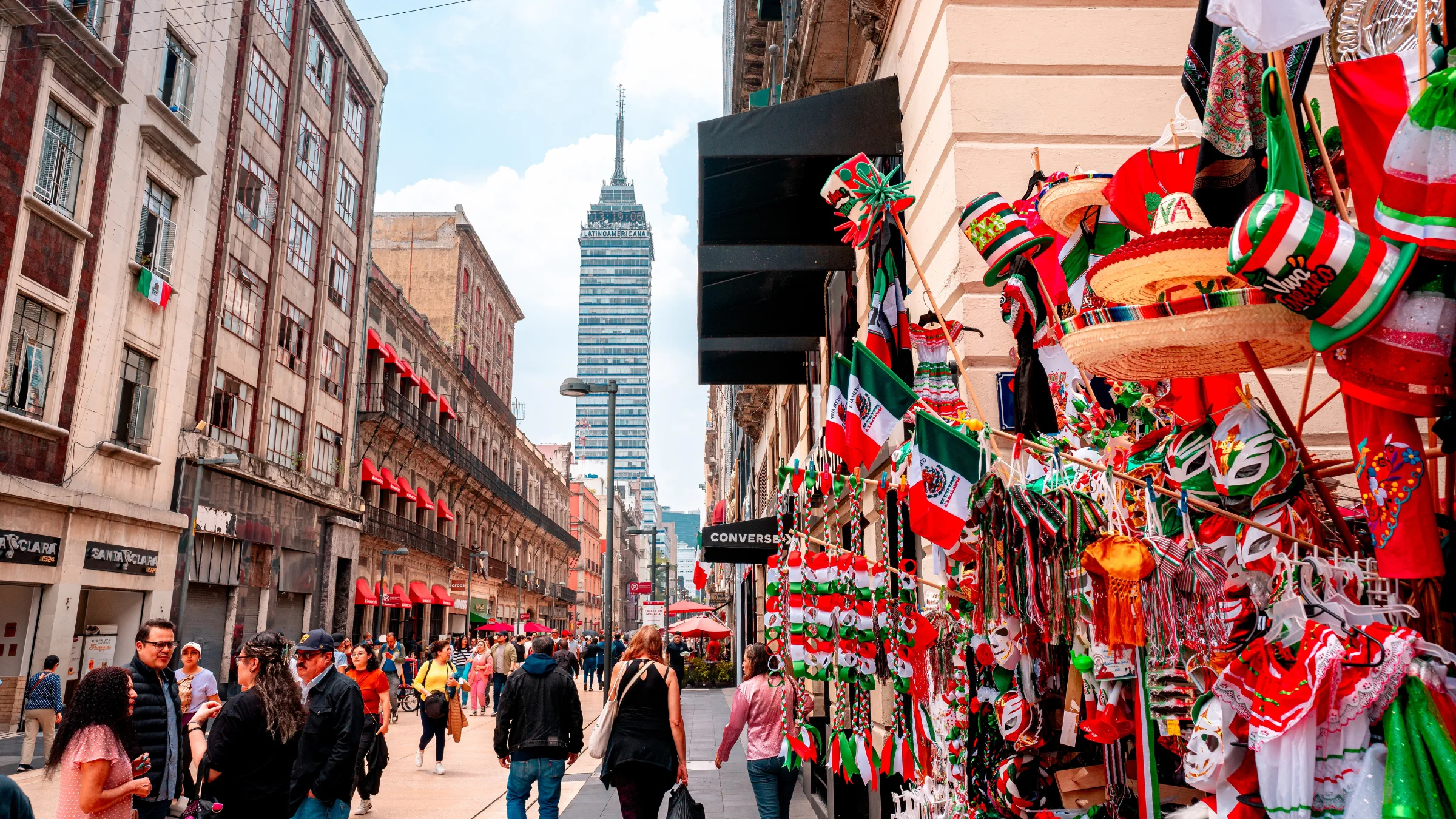 Busy Mexico City street lined with shops, pedestrians, and Mexican-themed souvenirs beneath the Torre Latinoamericana.