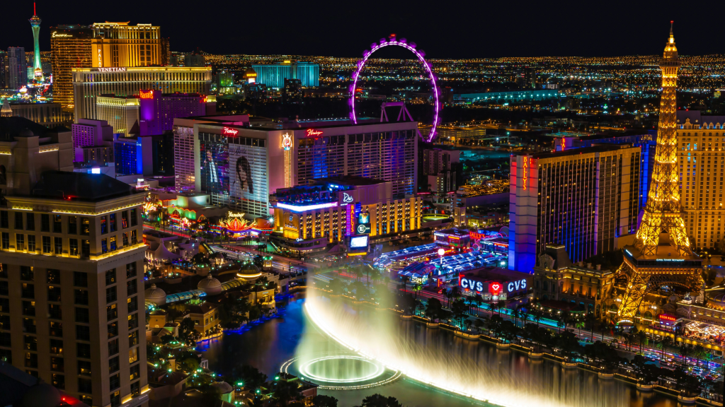Las Vegas Strip at night with bright casino lights, Bellagio fountains, and the High Roller in the distance.