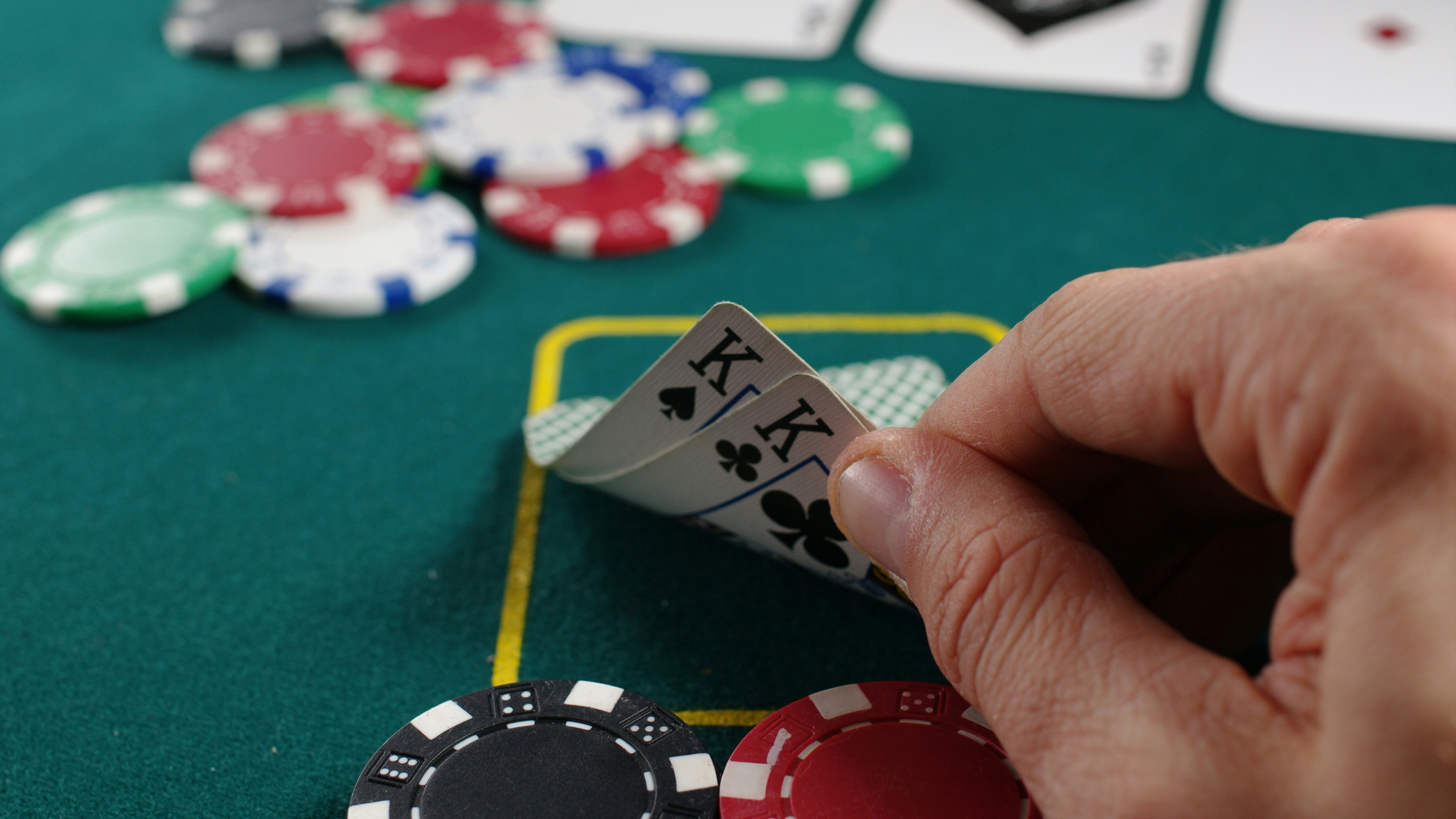 Close-up of a poker player lifting two king cards beside chips on a green felt table.