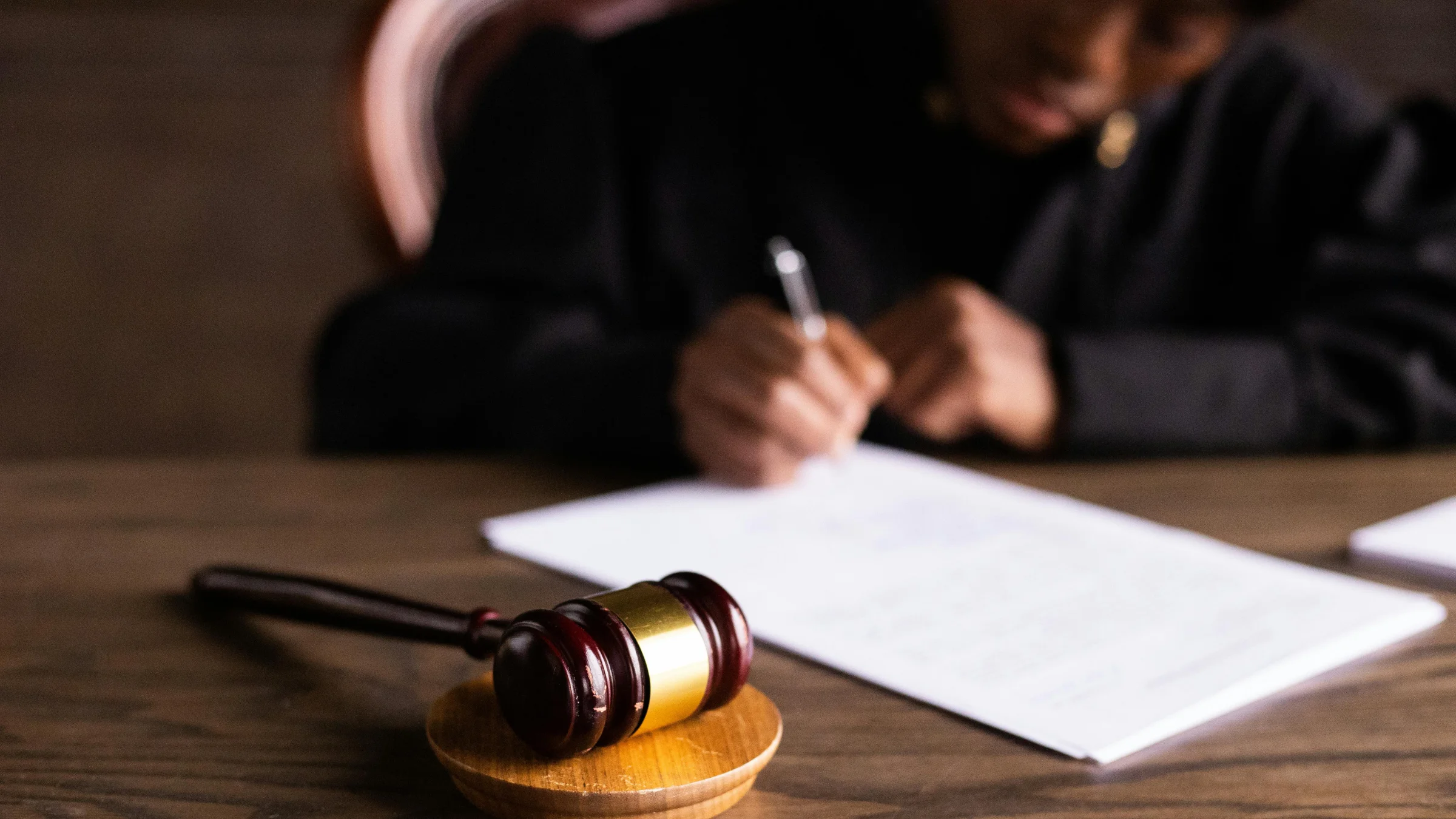 Judge’s gavel on a desk with a blurred person signing documents in the background.