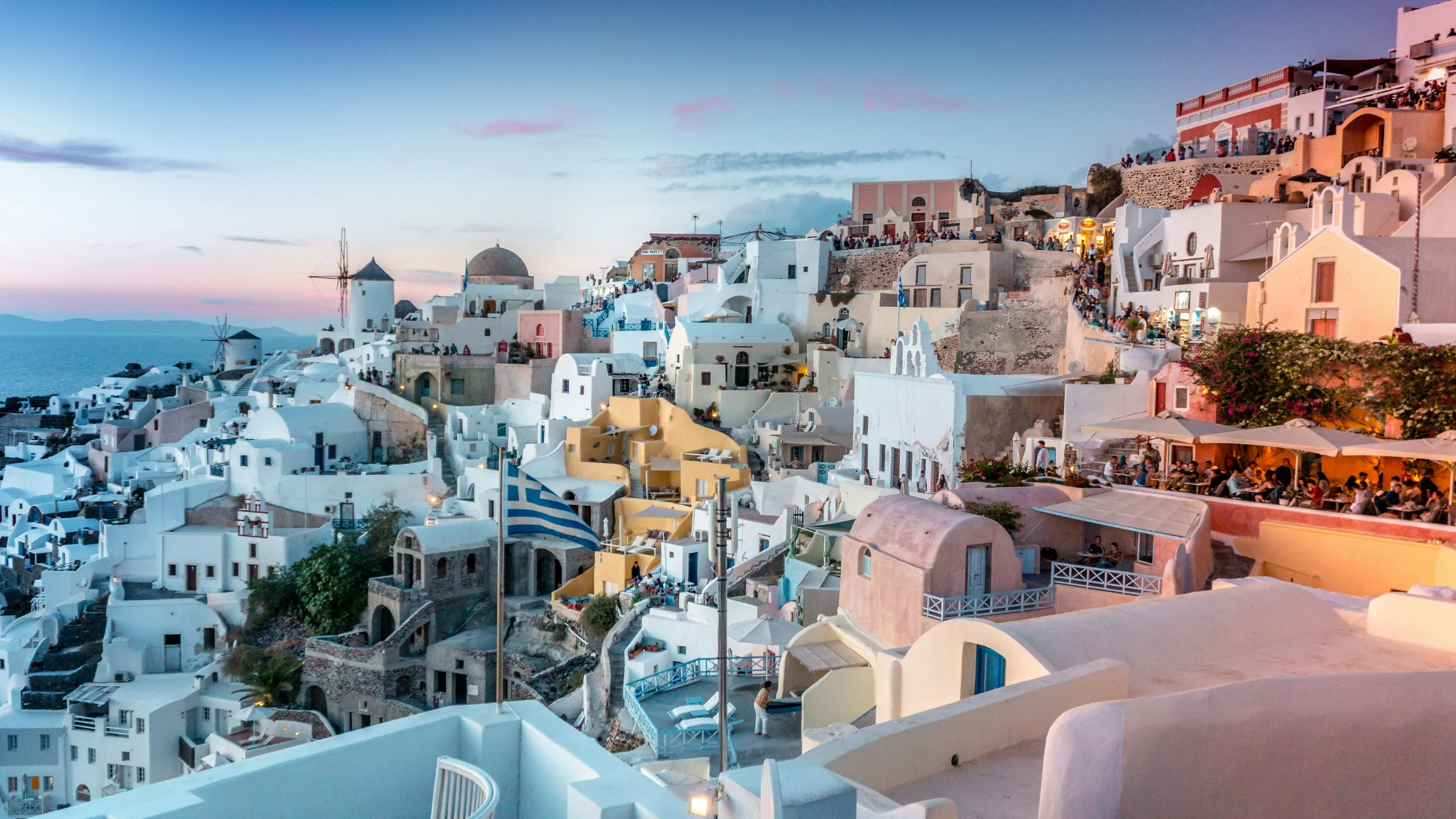 Santorini hillside at sunset with whitewashed buildings overlooking the Aegean Sea.