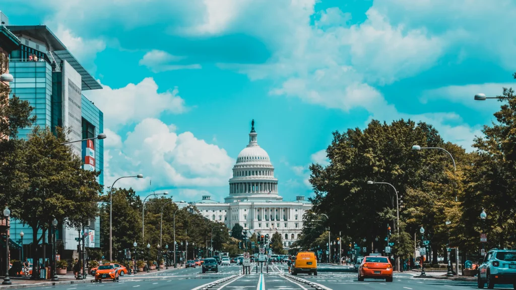 United States Capitol building viewed from a city street lined with trees and traffic.