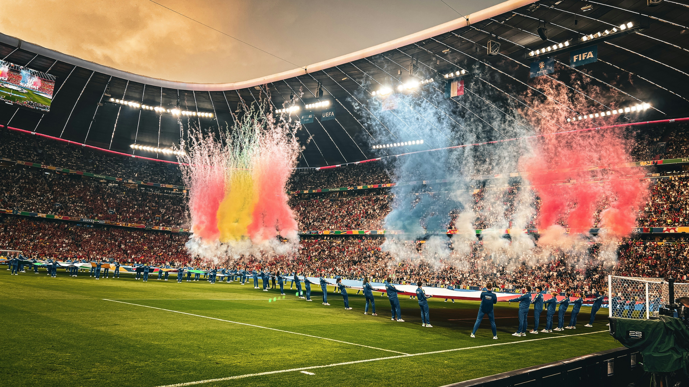 Packed soccer stadium during a pre-match ceremony with colorful smoke rising above the field.