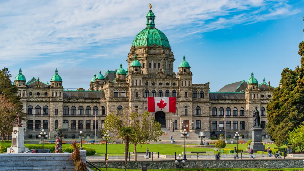 Historic parliament building with green domes and a Canadian flag displayed at the front.