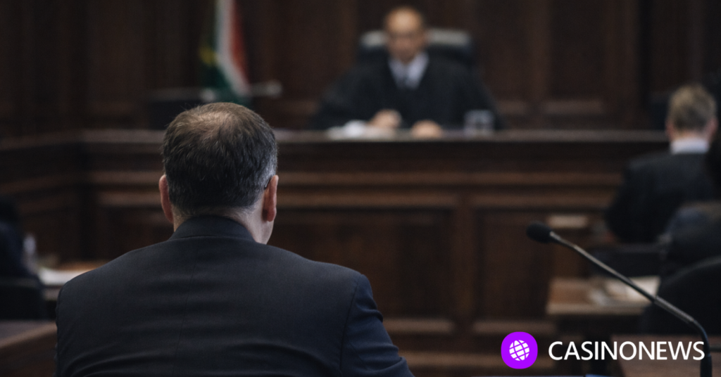 Man seated at a courtroom hearing facing a judge, representing the Investec R2.6 million online gambling debt case.