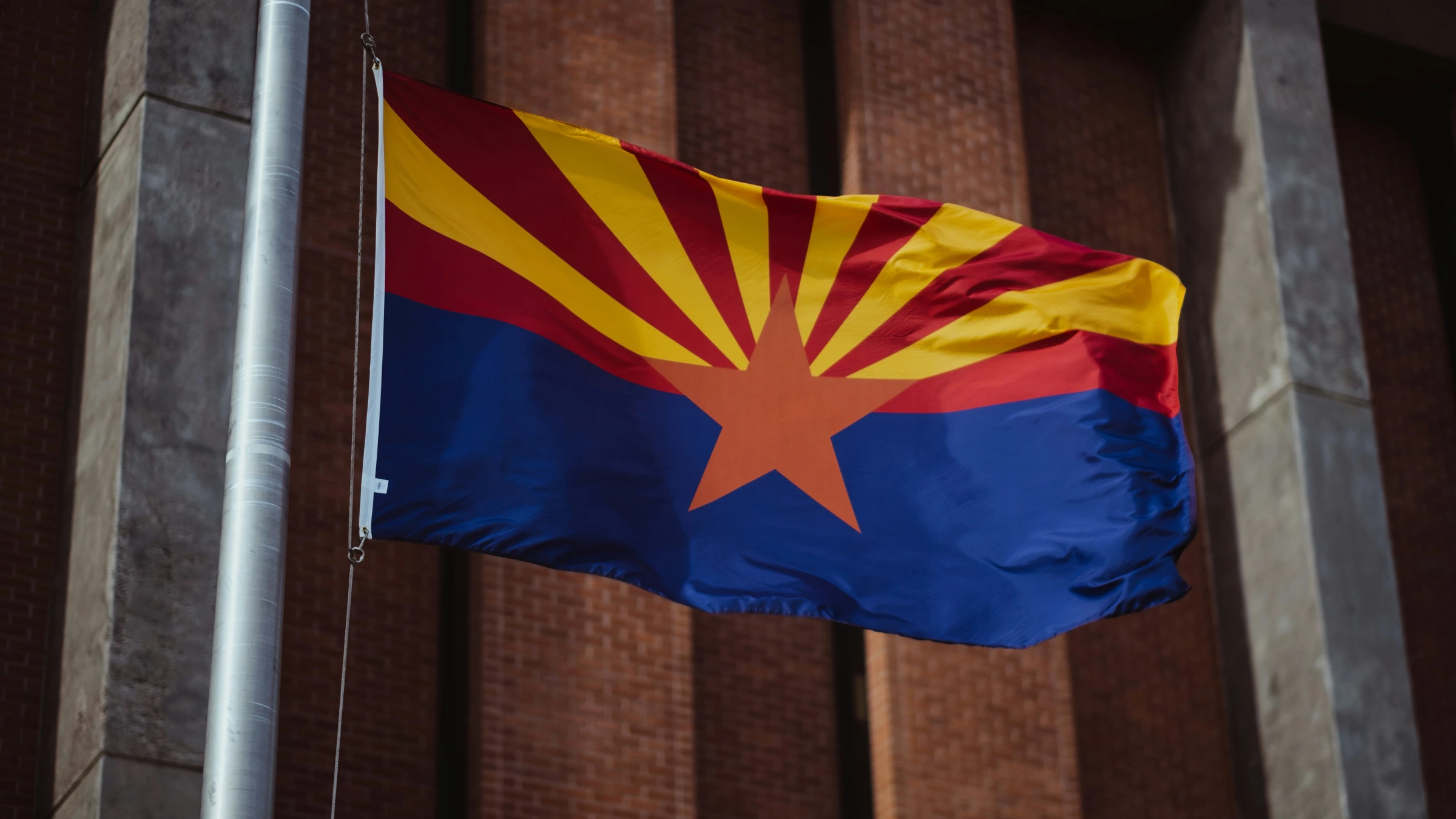 Arizona state flag waving on a flagpole in front of a building
