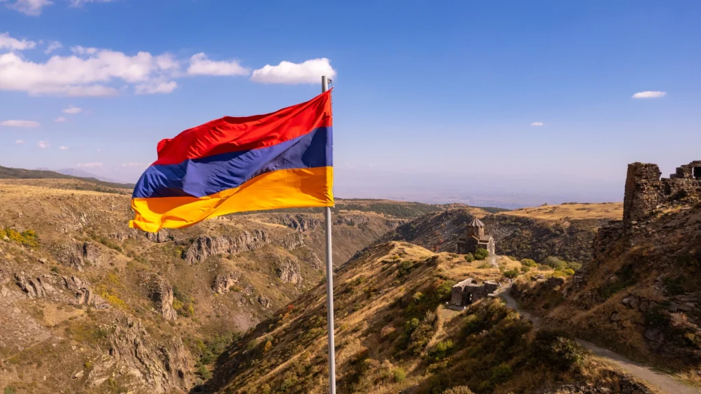 Armenian national flag flying above rocky mountain landscape with historic monastery in background