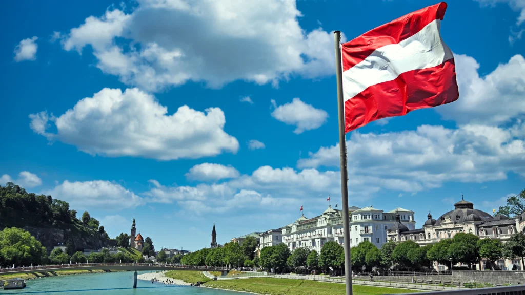 Austrian national flag flying above riverside city district under bright blue sky