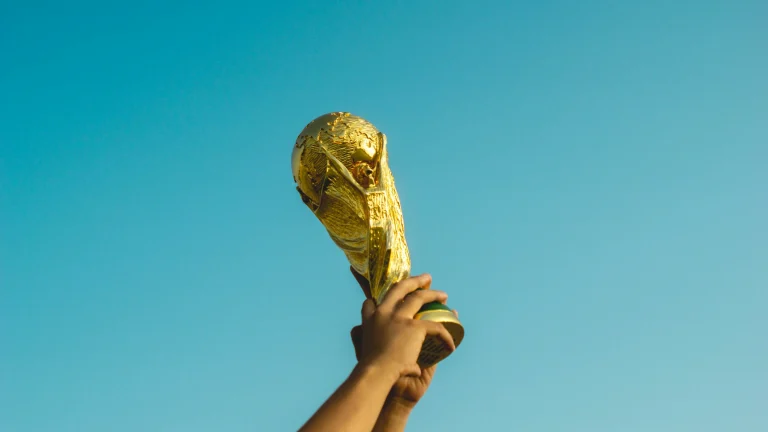 Hands holding FIFA World Cup trophy aloft against clear sky before tournament