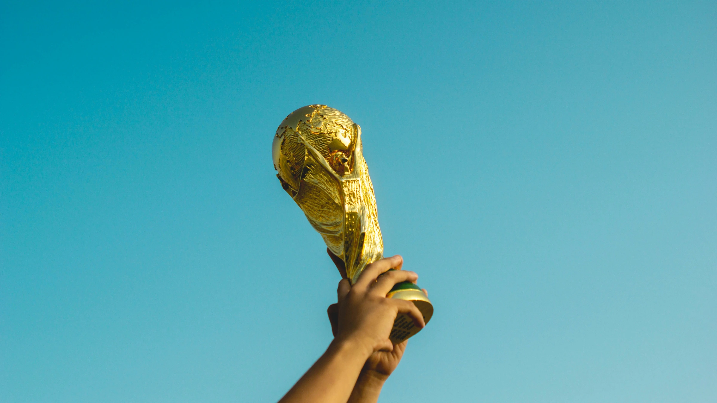 Hands holding FIFA World Cup trophy aloft against clear sky before tournament
