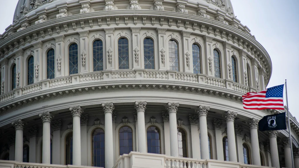 Exterior view of United States Capitol dome with columns and American flag flying in front.