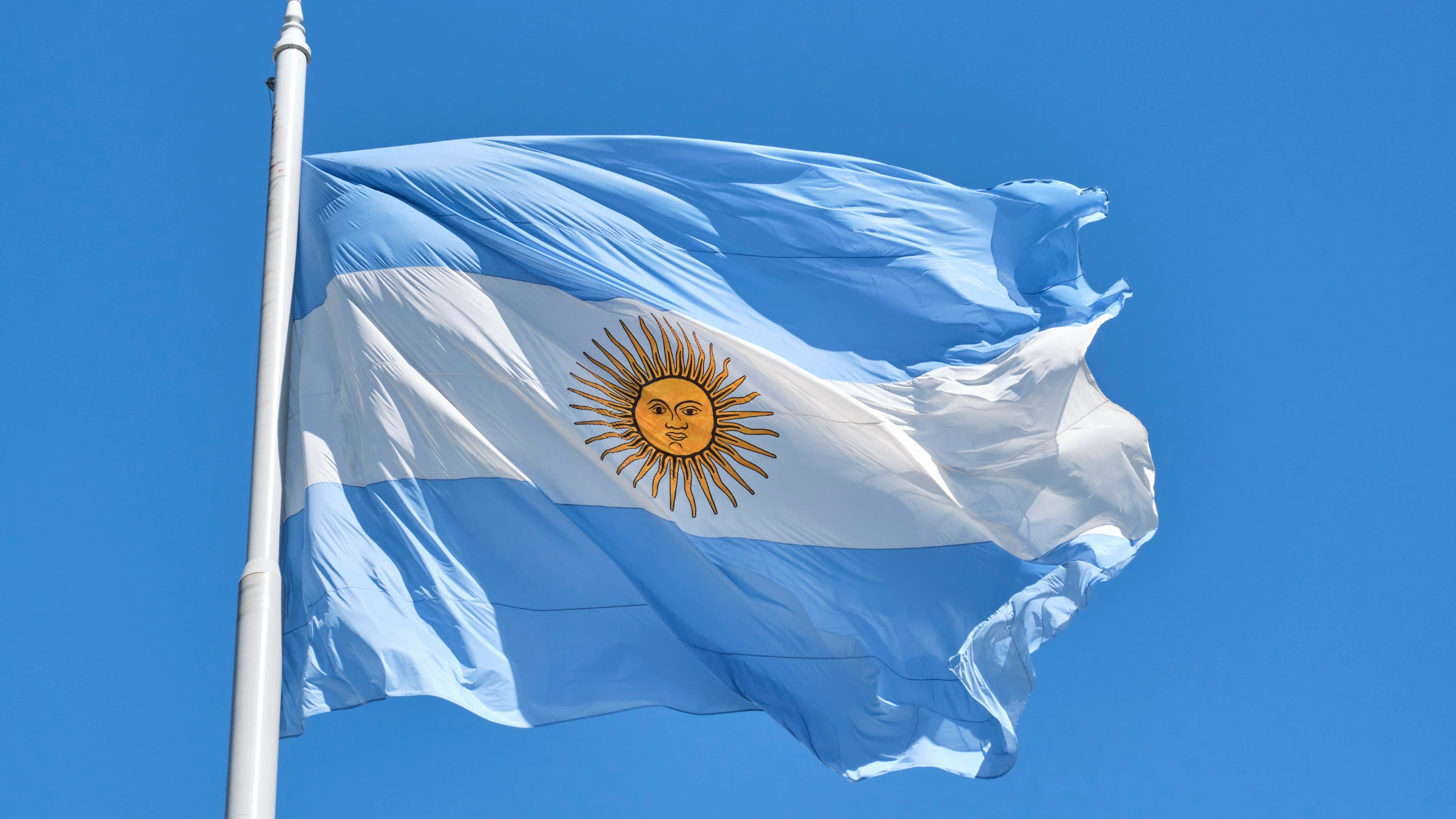 Argentine national flag waving on tall flagpole against clear blue sky