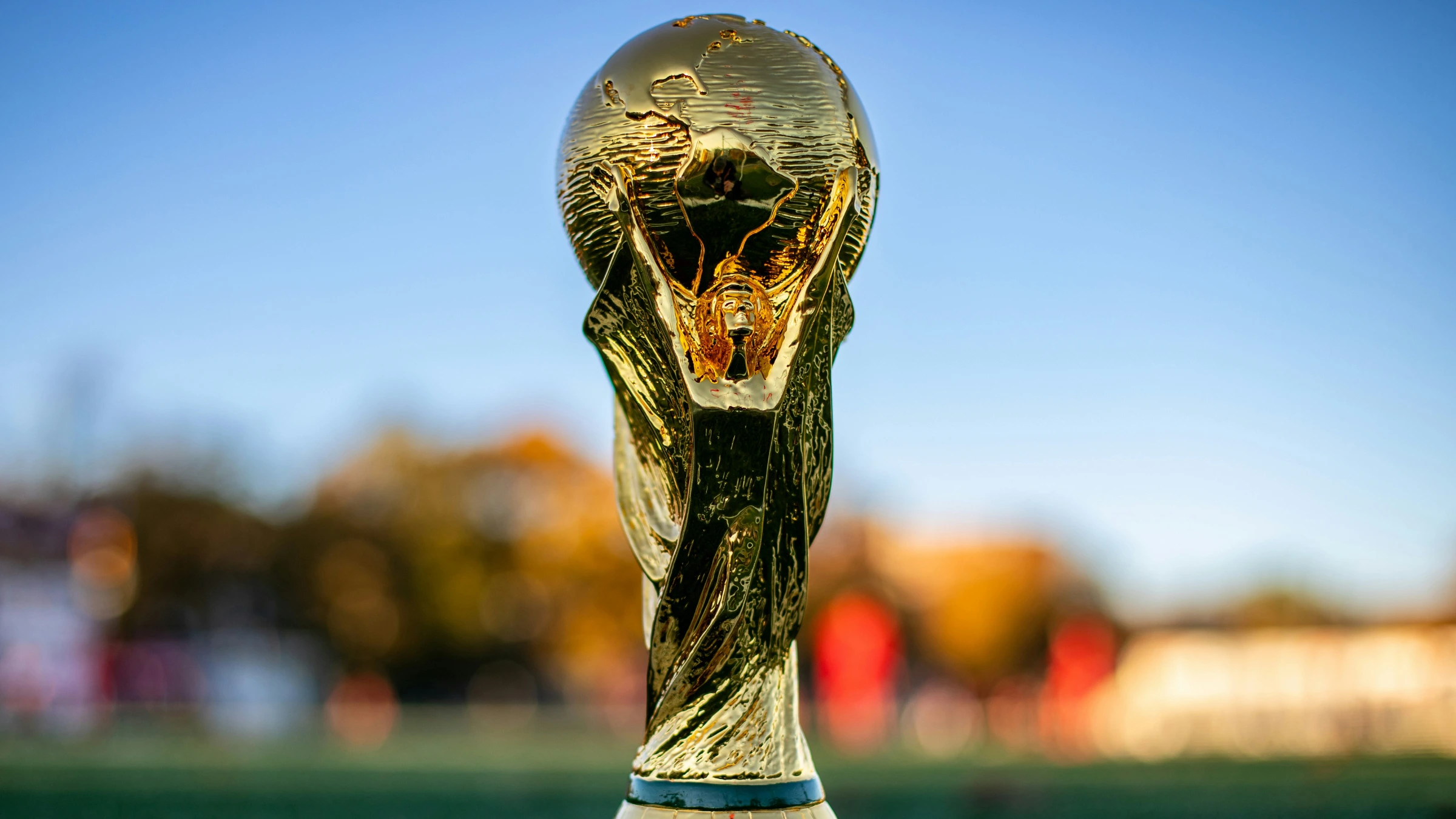 Close-up of golden FIFA World Cup trophy standing on field with blurred background.