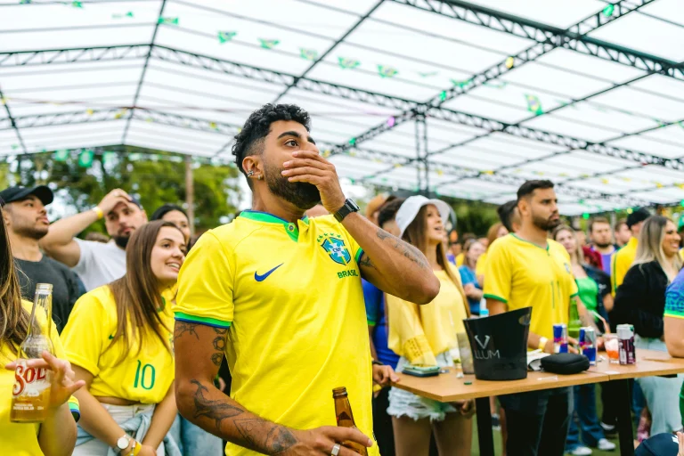 Group of Brazil football fans in yellow jerseys watching match outdoors, reacting with surprise and concern.