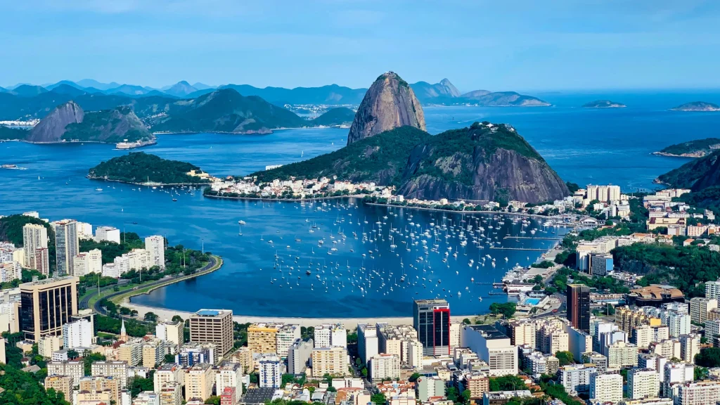 Aerial view of Rio de Janeiro with Sugarloaf Mountain, coastline, boats, and dense city skyline.