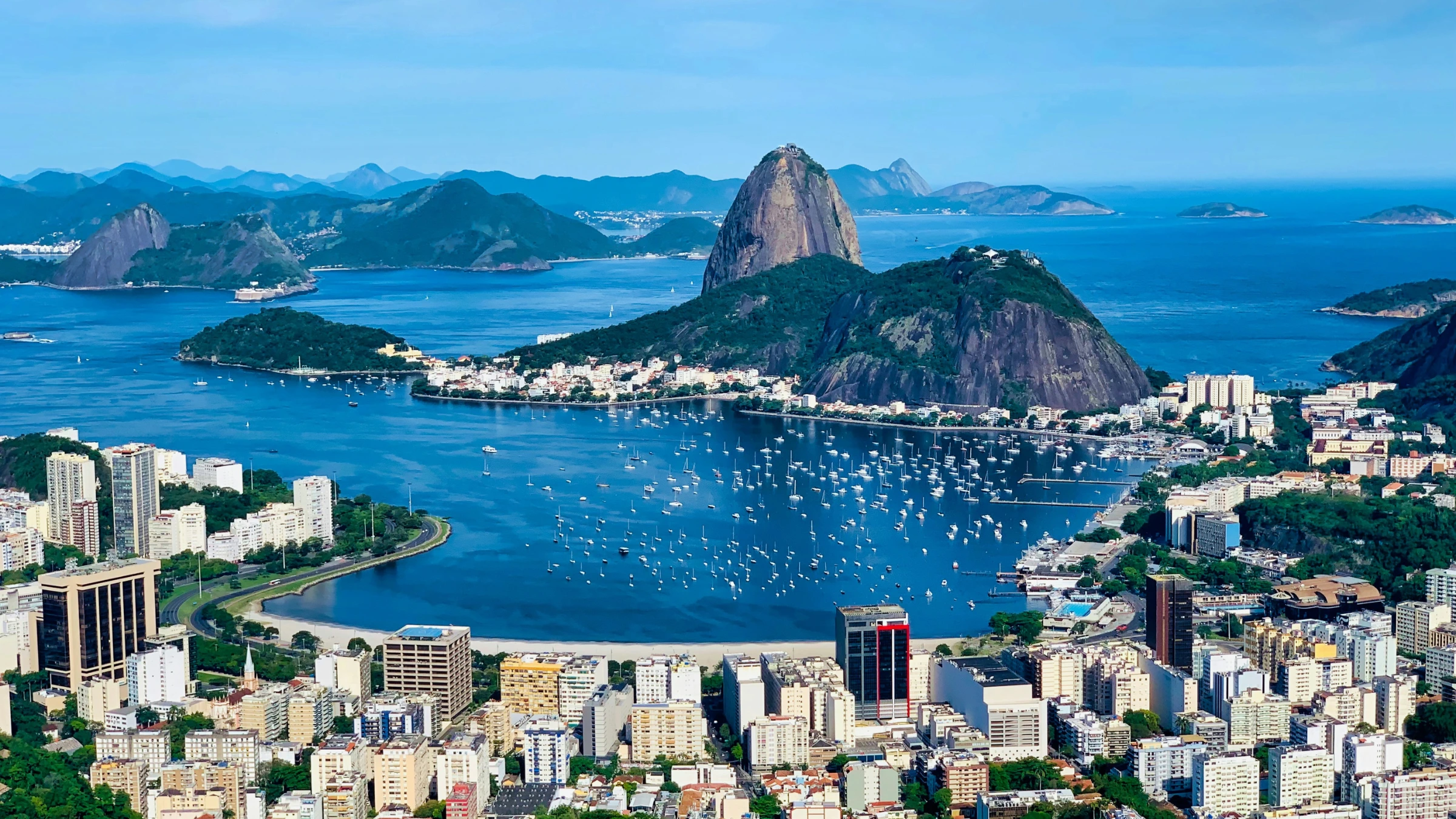 Aerial view of Rio de Janeiro with Sugarloaf Mountain, coastline, boats, and dense city skyline.