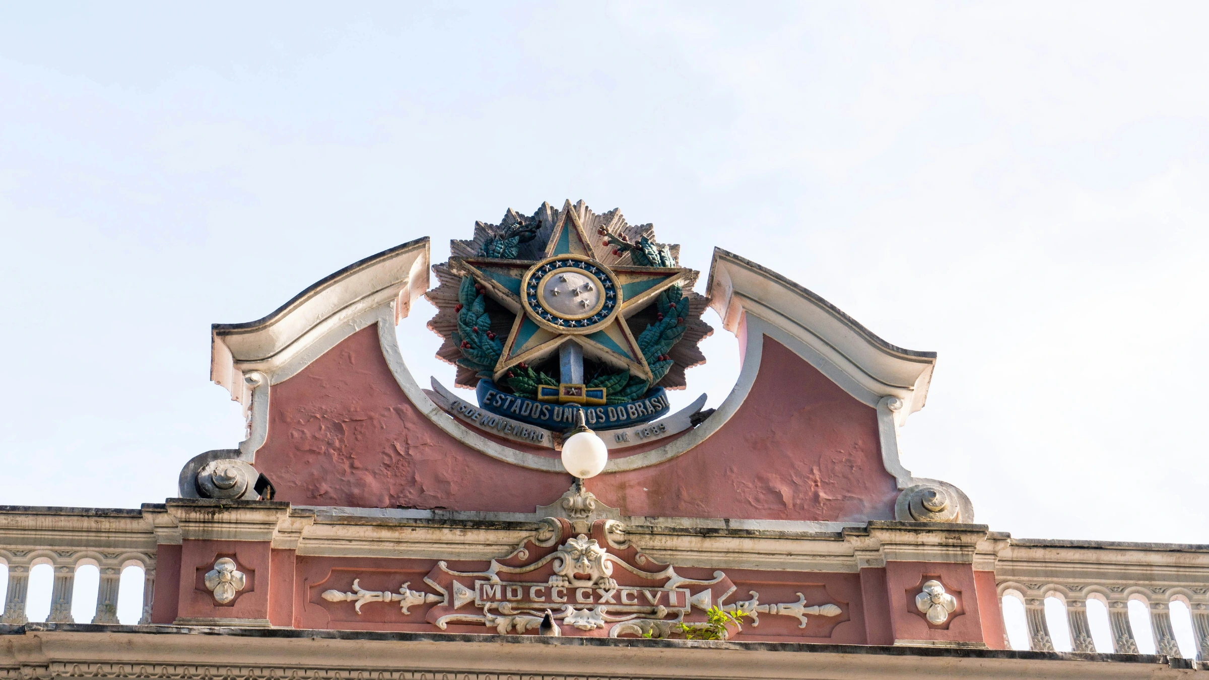 Close-up of ornate Brazilian coat of arms mounted on historic building facade against clear sky.