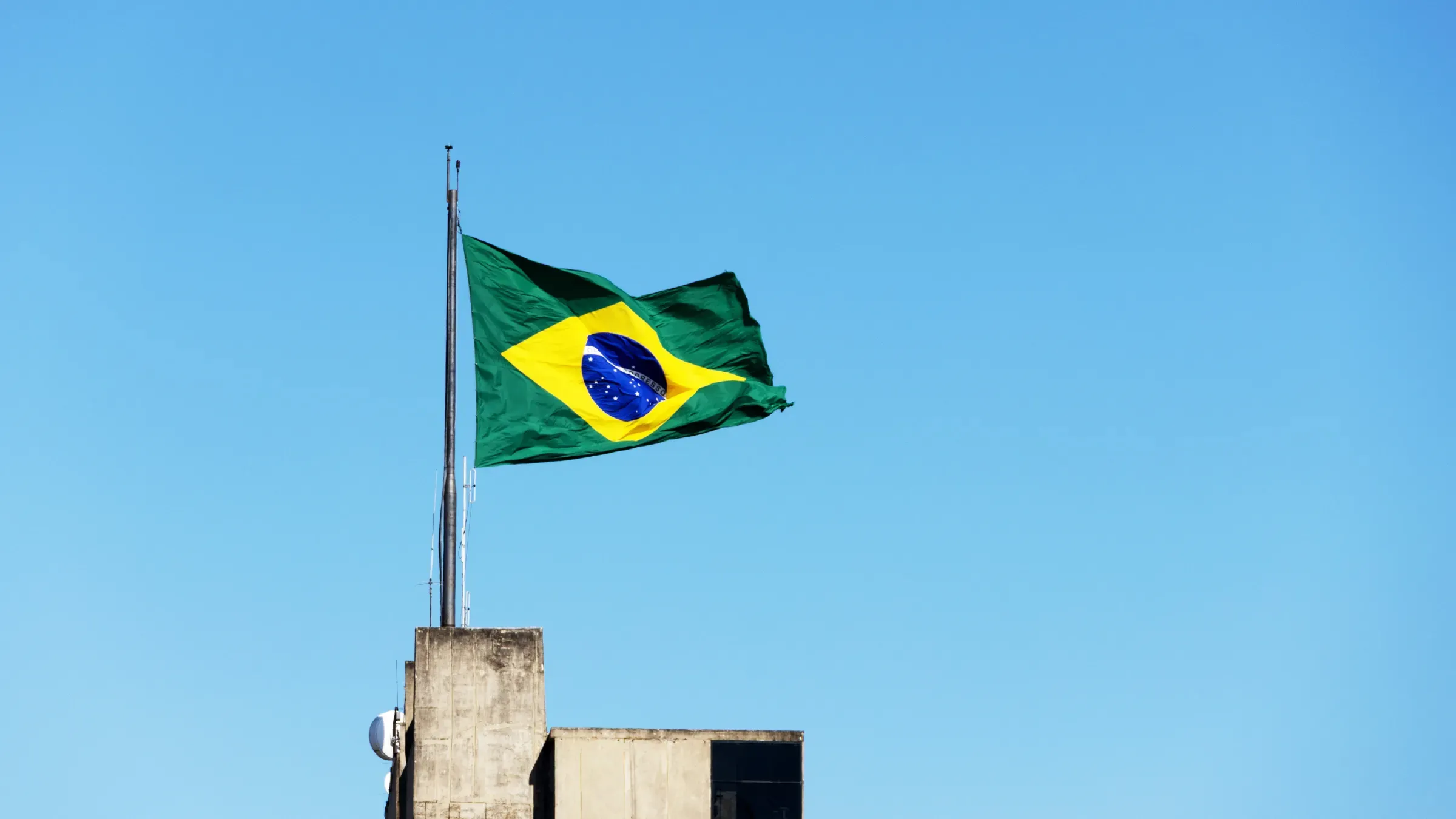 Brazilian flag waving above rooftop against bright blue sky