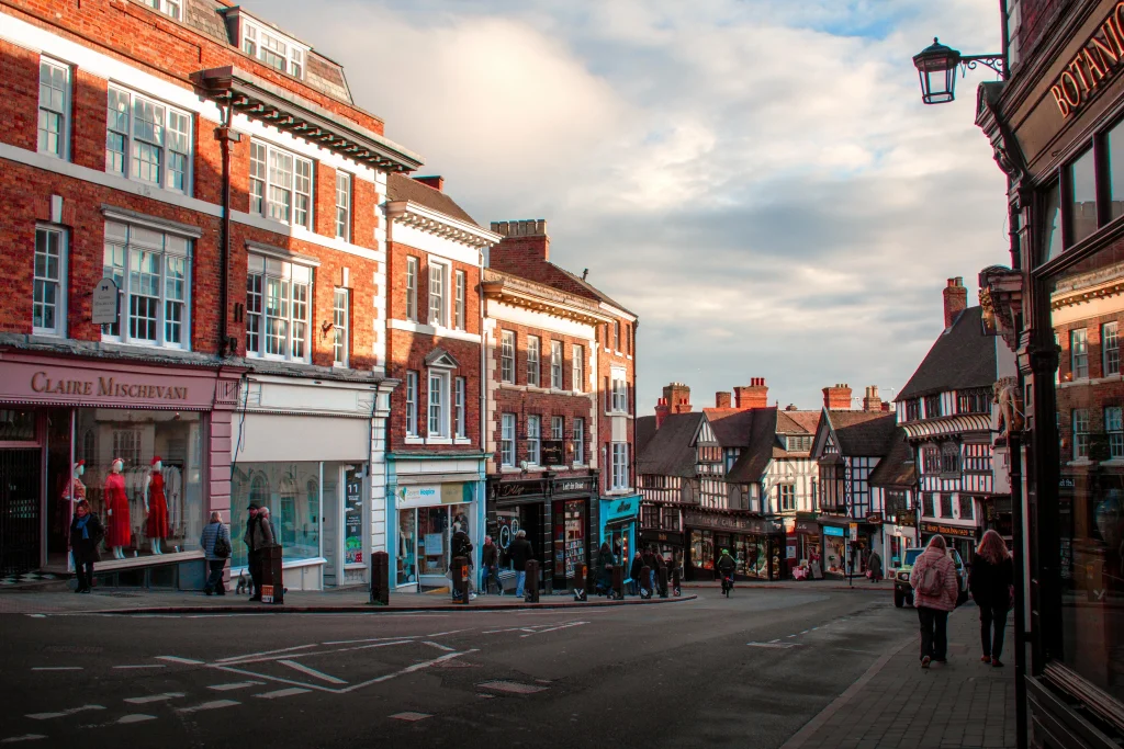 Historic town street with brick buildings, shopfronts, and pedestrians walking along a curved road.