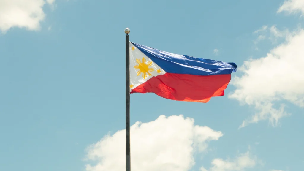 Philippine national flag flying on flagpole against bright blue sky