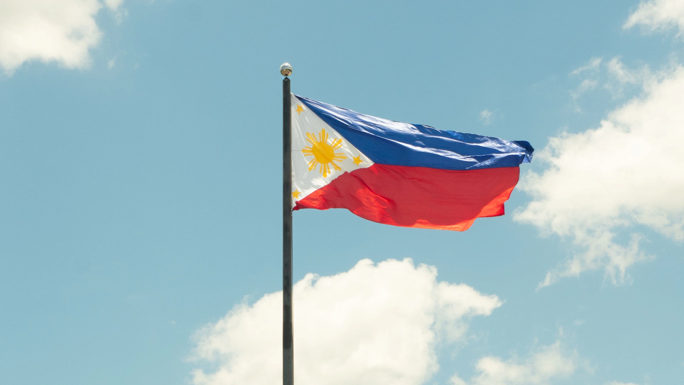 Philippine national flag flying on flagpole against bright blue sky