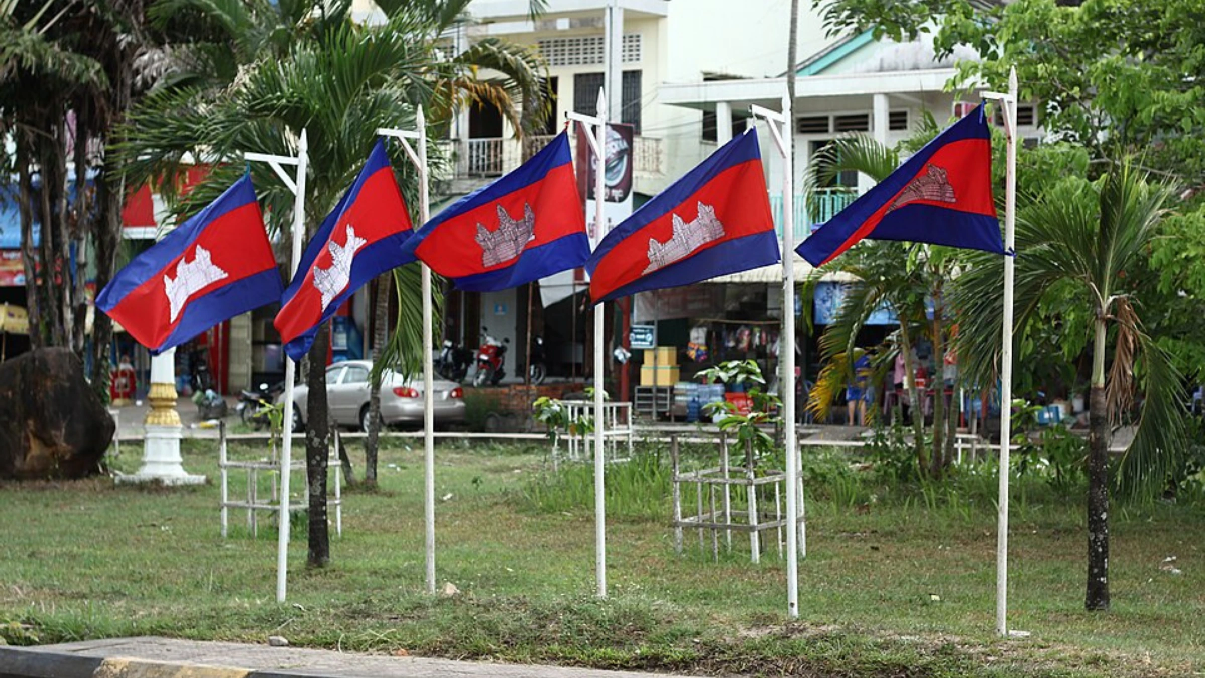 Multiple Cambodian national flags displayed along a landscaped urban street