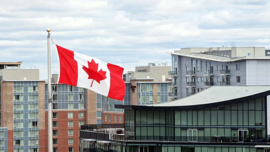 Canadian flag waving above modern city buildings under cloudy sky
