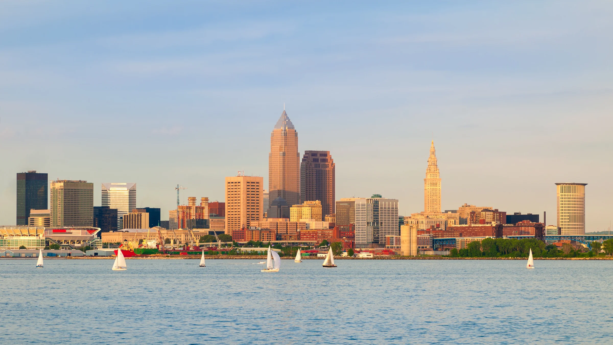 Cleveland skyline viewed across the water with sailboats in the foreground during golden-hour light.