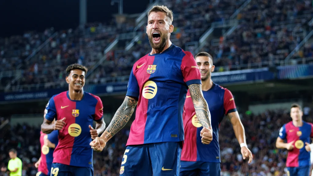 Barcelona players celebrate on the pitch during a night match in front of a packed stadium crowd.