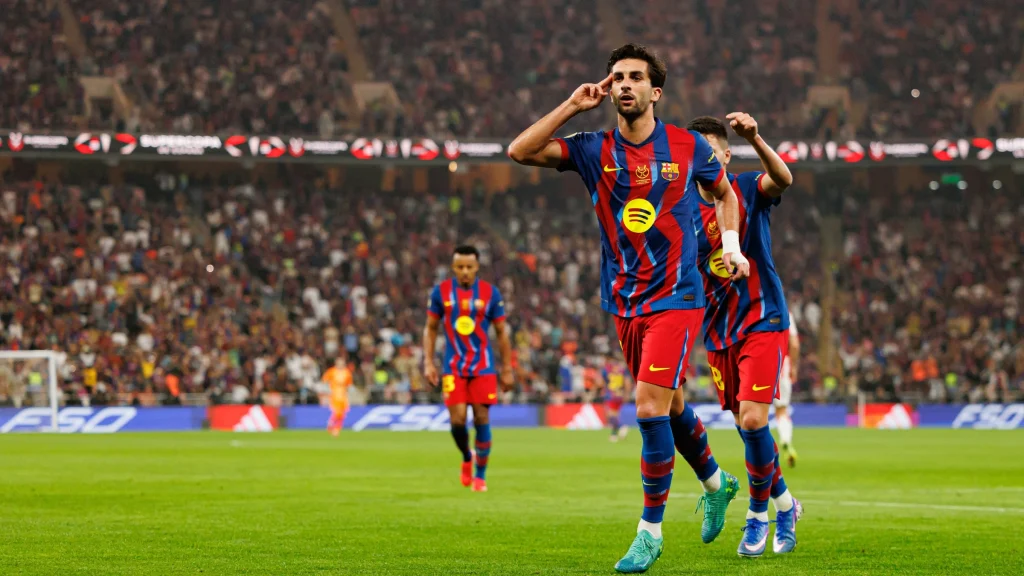 Barcelona players celebrate on the pitch during a packed night match after scoring.