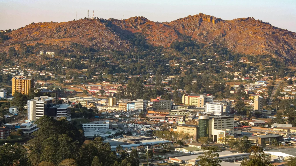 Cityscape with low-rise buildings and hillside terrain covered with rocky slopes and scattered houses.