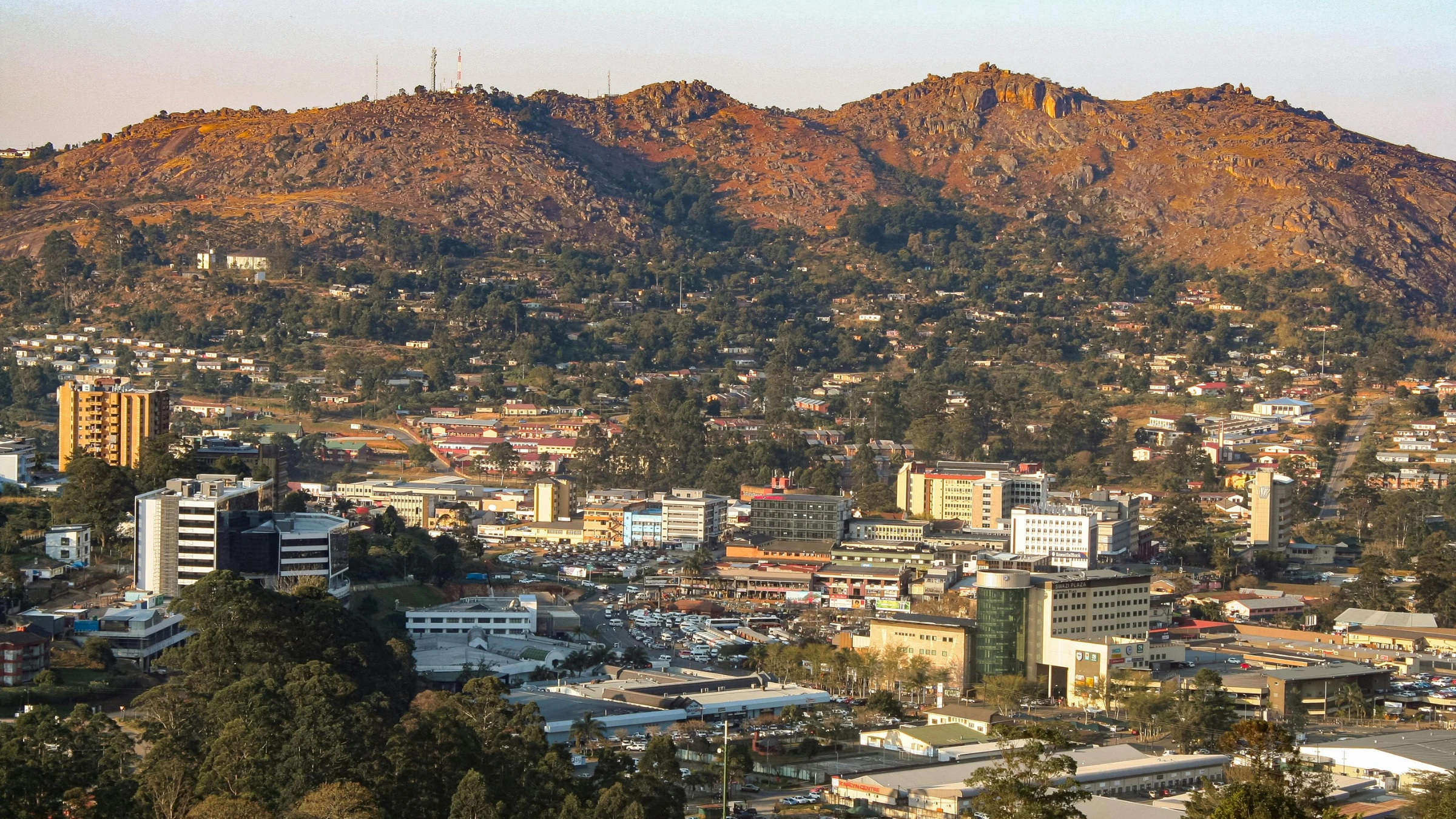 Cityscape with low-rise buildings and hillside terrain covered with rocky slopes and scattered houses.