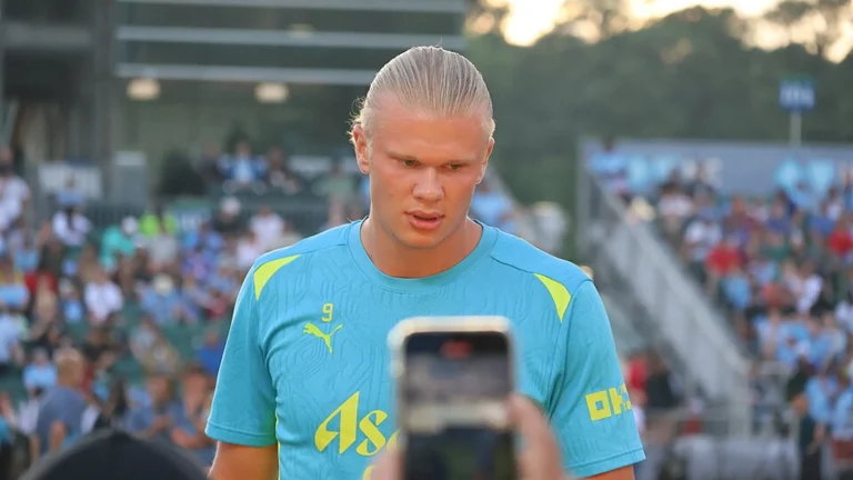 Football striker in training kit walks past crowd at sports venue