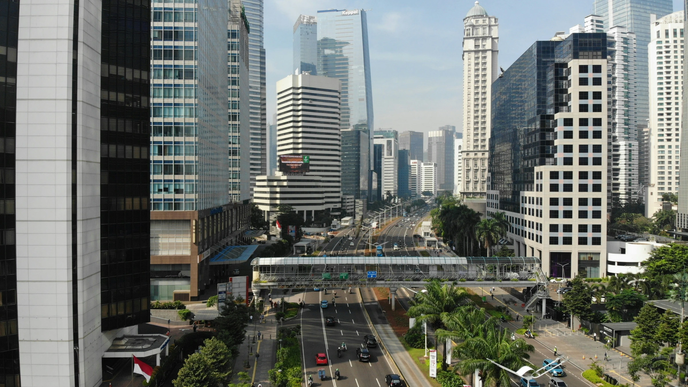Modern city street with tall office buildings, traffic lanes, and pedestrian bridge crossing roadway.
