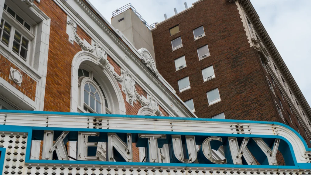 Close-up view of Kentucky theatre sign on building facade with brick structure and windows above.