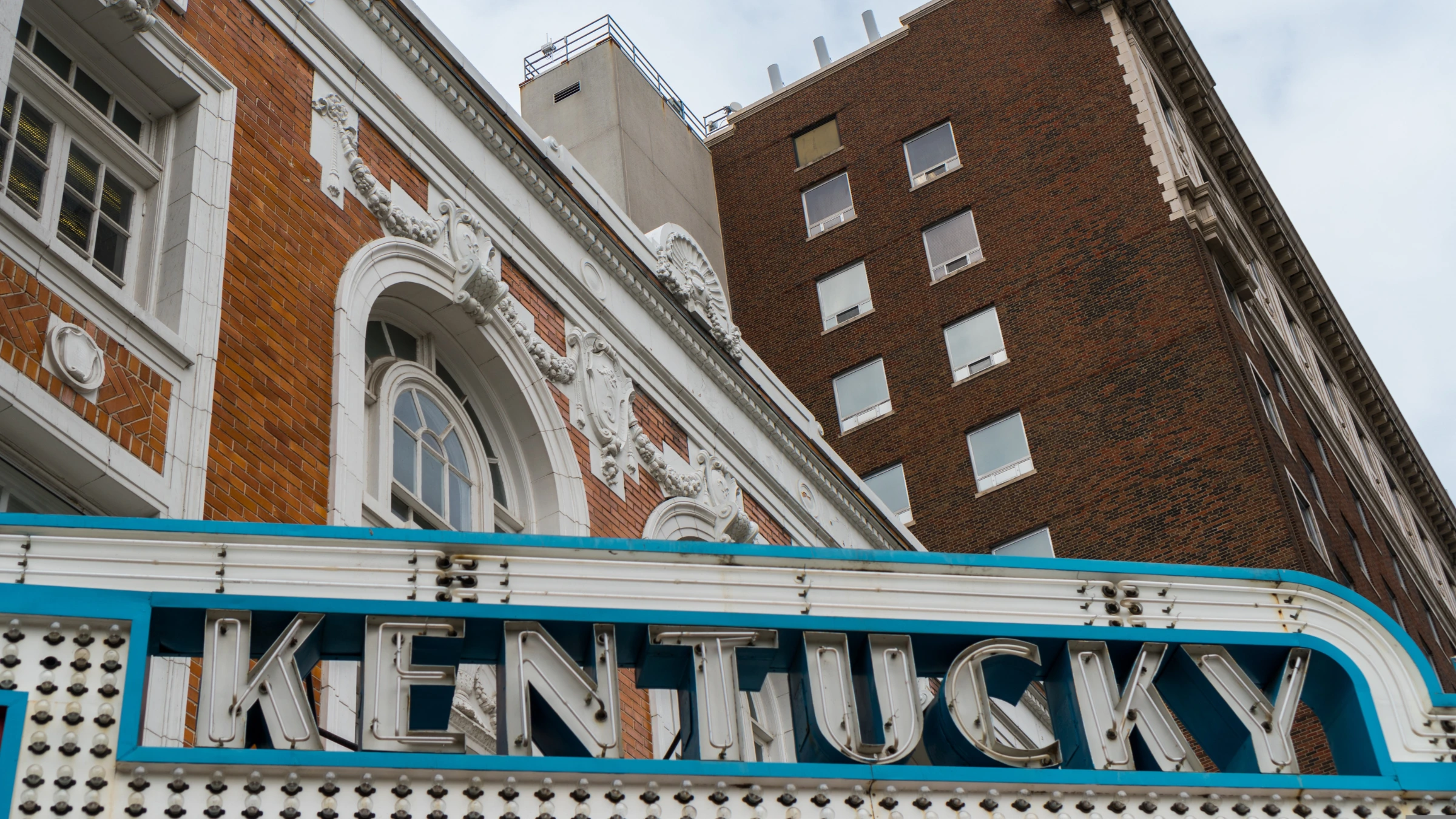 Close-up view of Kentucky theatre sign on building facade with brick structure and windows above.
