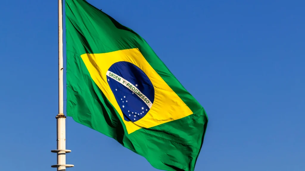Brazilian national flag waving on flagpole against bright blue sky during daytime