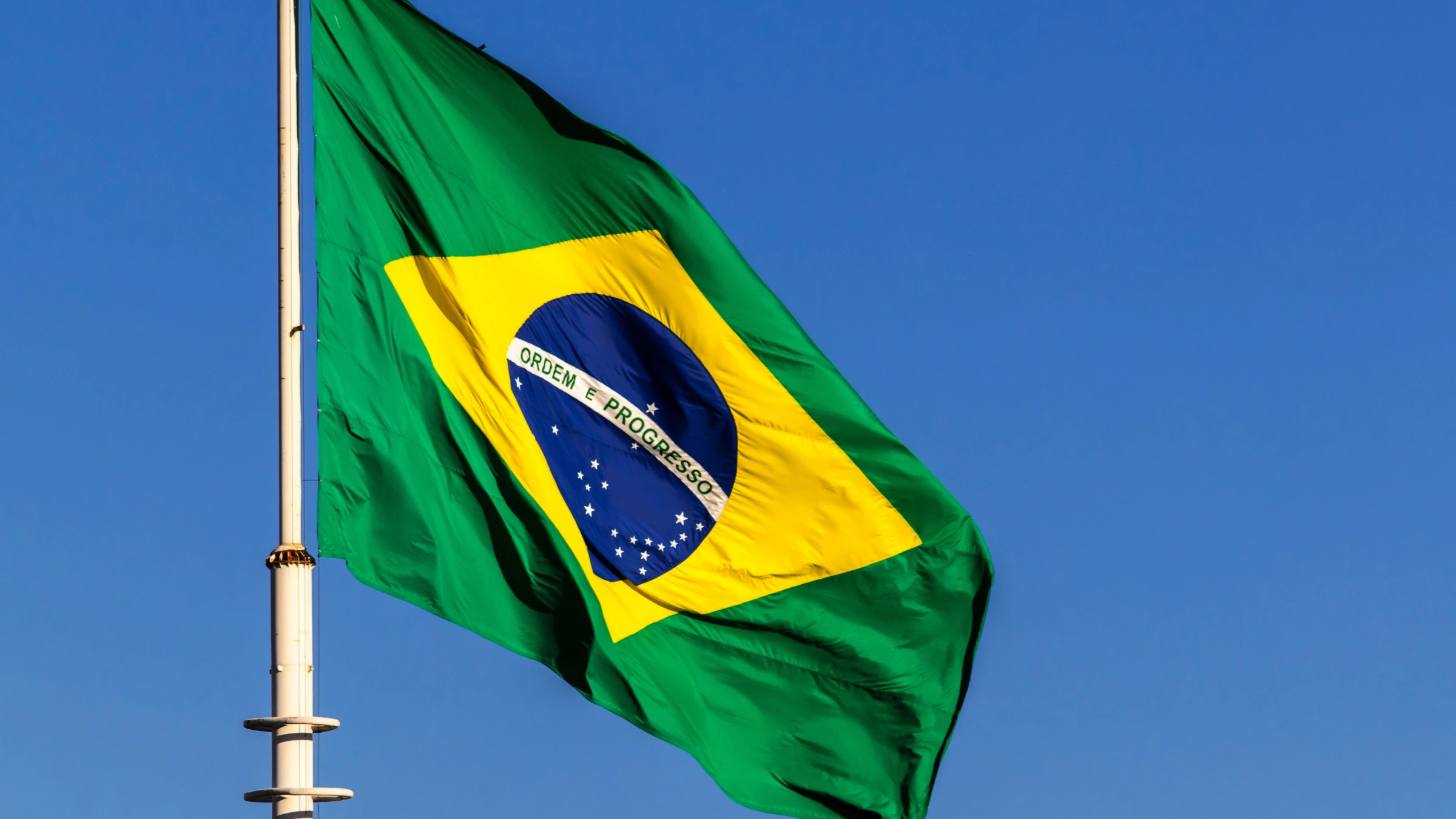 Brazilian national flag waving on flagpole against bright blue sky during daytime