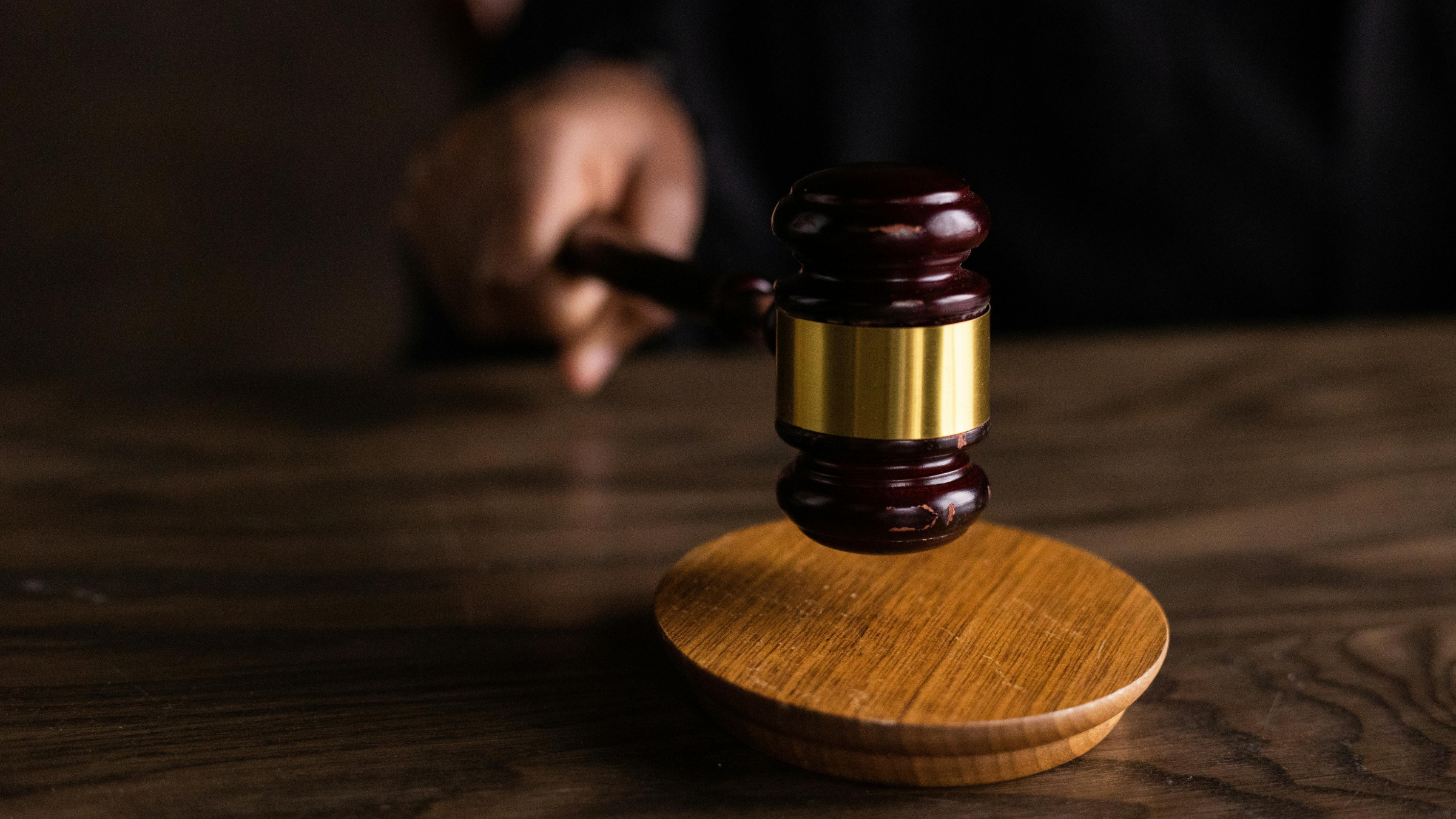 Close-up of a judge’s gavel striking a wooden sound block on a courtroom desk.