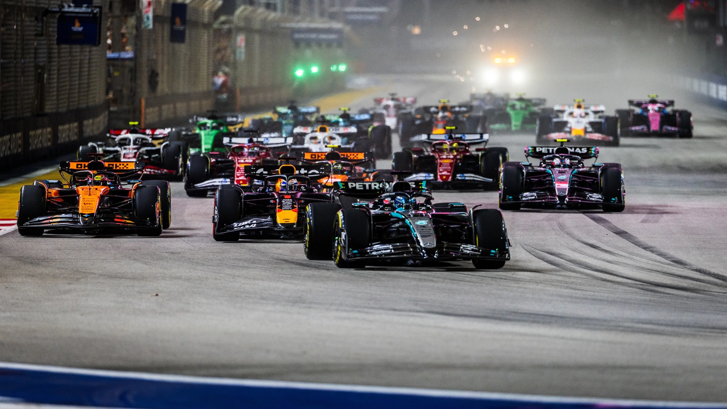 Formula 1 cars race side by side on a floodlit circuit during a night Grand Prix.