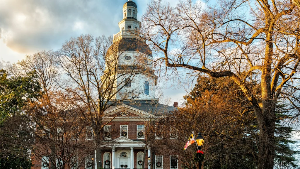 Historic government building with domed tower and brick facade framed by leafless trees at sunset.