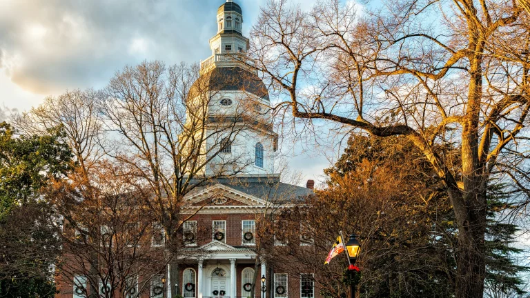 Historic government building with domed tower and brick facade framed by leafless trees at sunset.