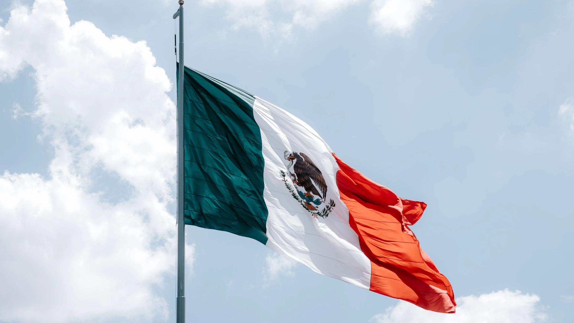 Mexican national flag waving on flagpole beneath bright cloudy sky