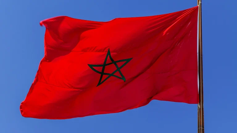 Moroccan national flag waving on a flagpole against a clear blue sky