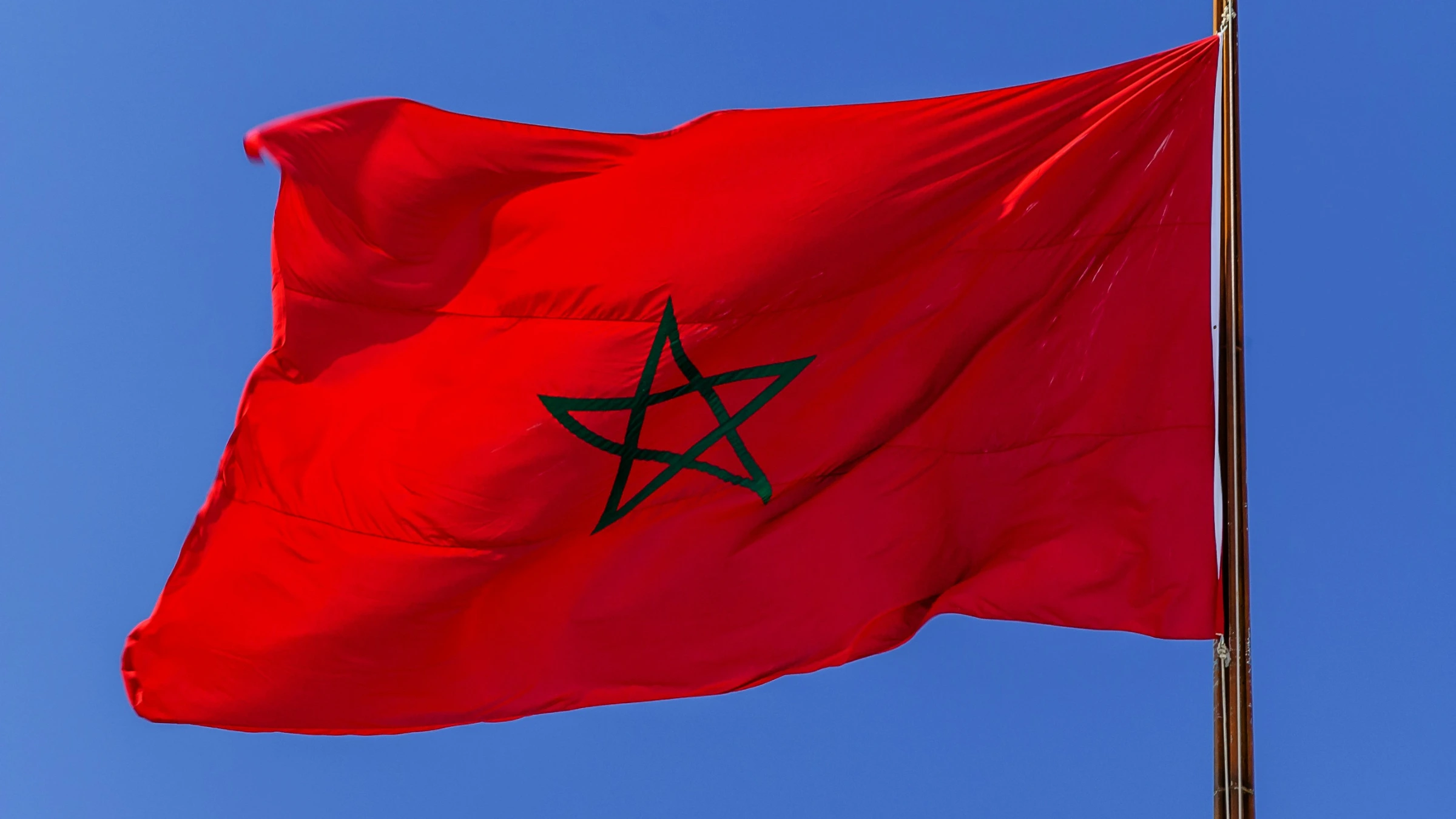 Moroccan national flag waving on a flagpole against a clear blue sky