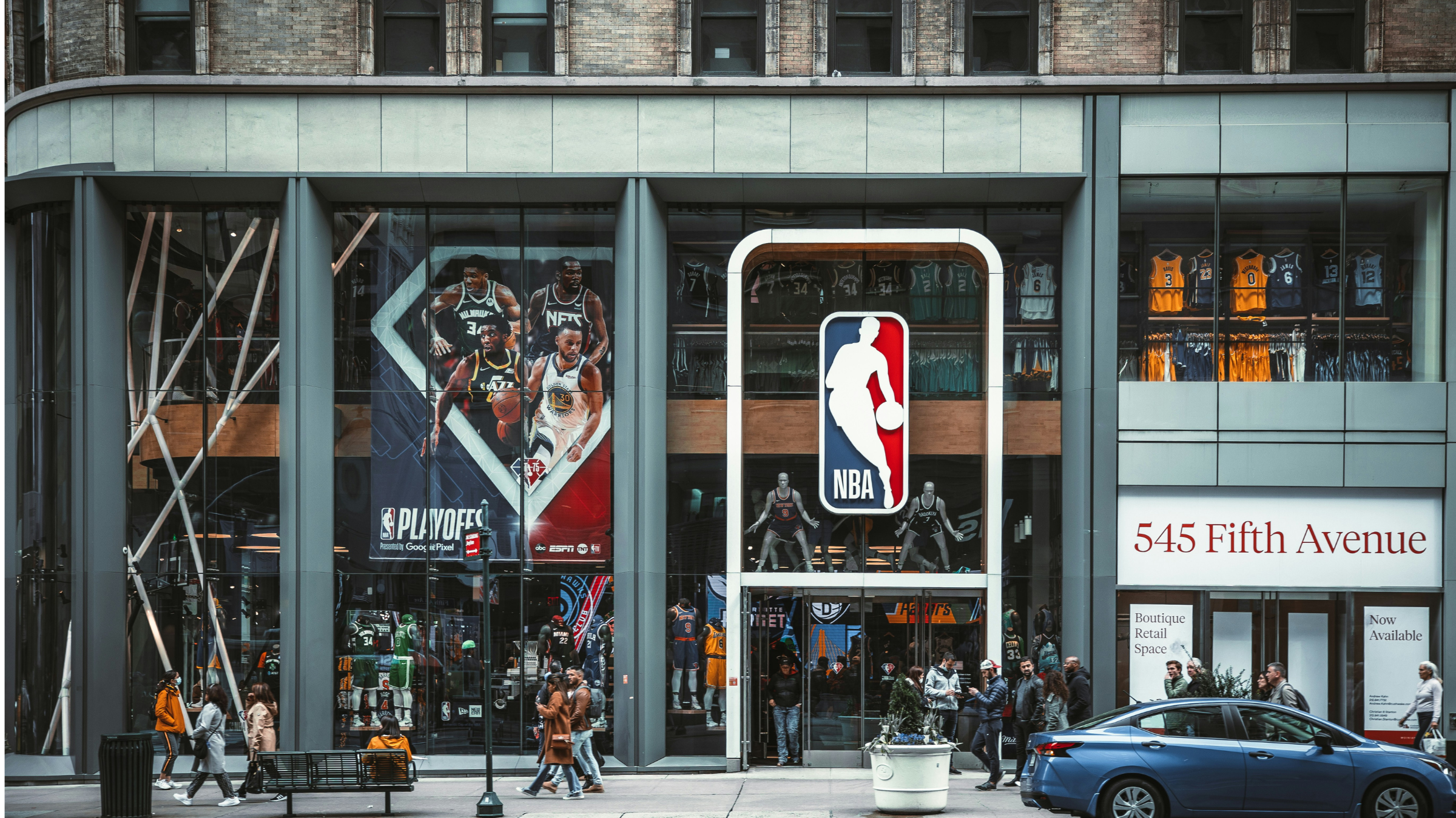 Street-level view of NBA Store entrance at 545 Fifth Avenue with pedestrians and parked cars.